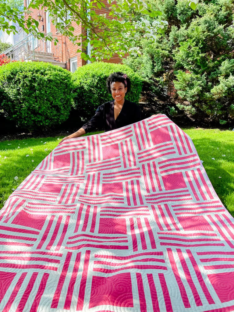 Person holding quilt pink and white stripes with pink squares in the middle.