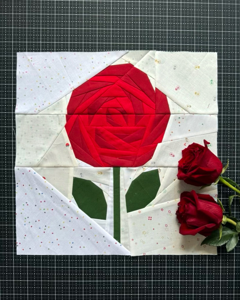 Quilt block with a red rose on a white background, accompanied by real roses.