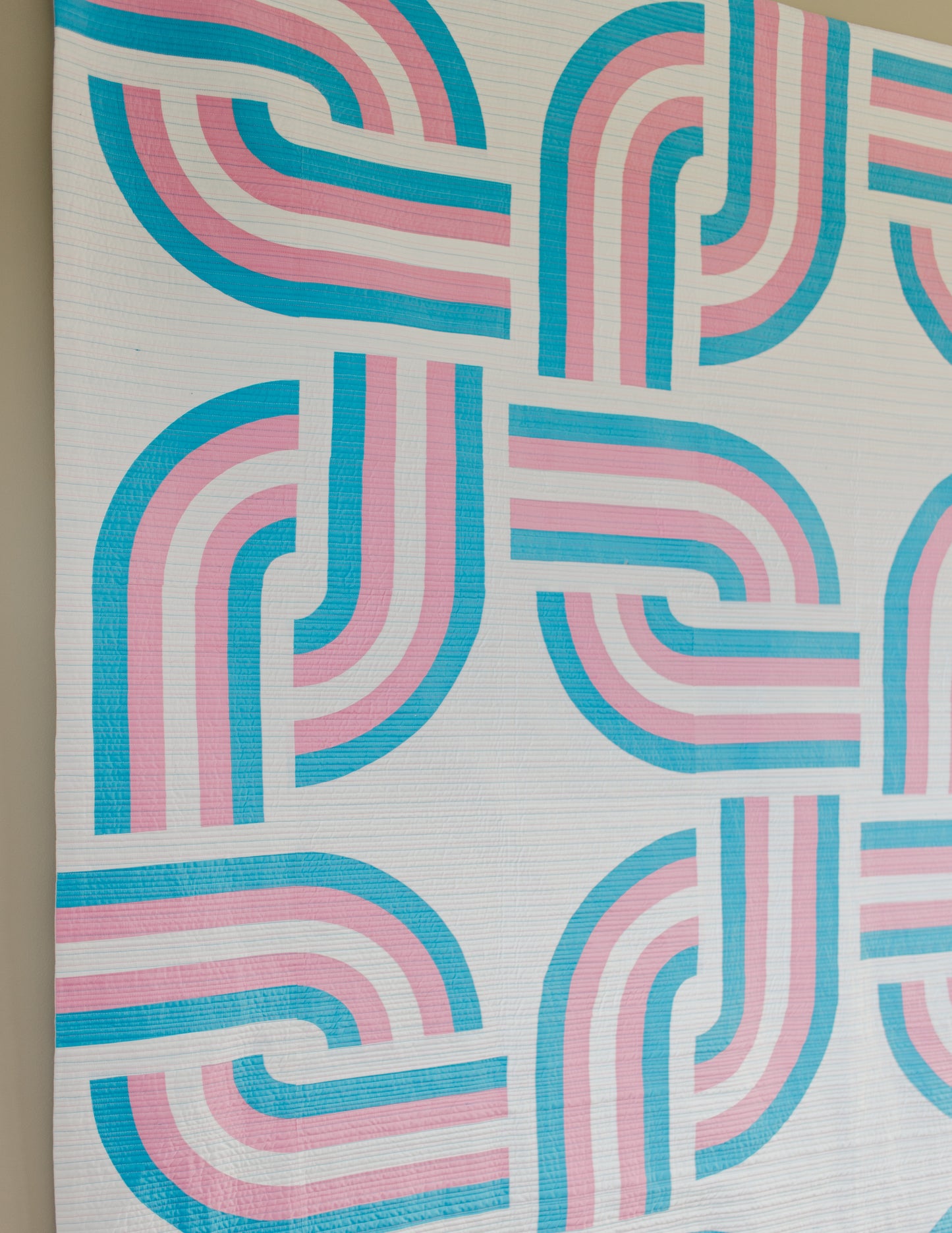 Close up view of quilt with pink and blue wavy pattern on a neutral background