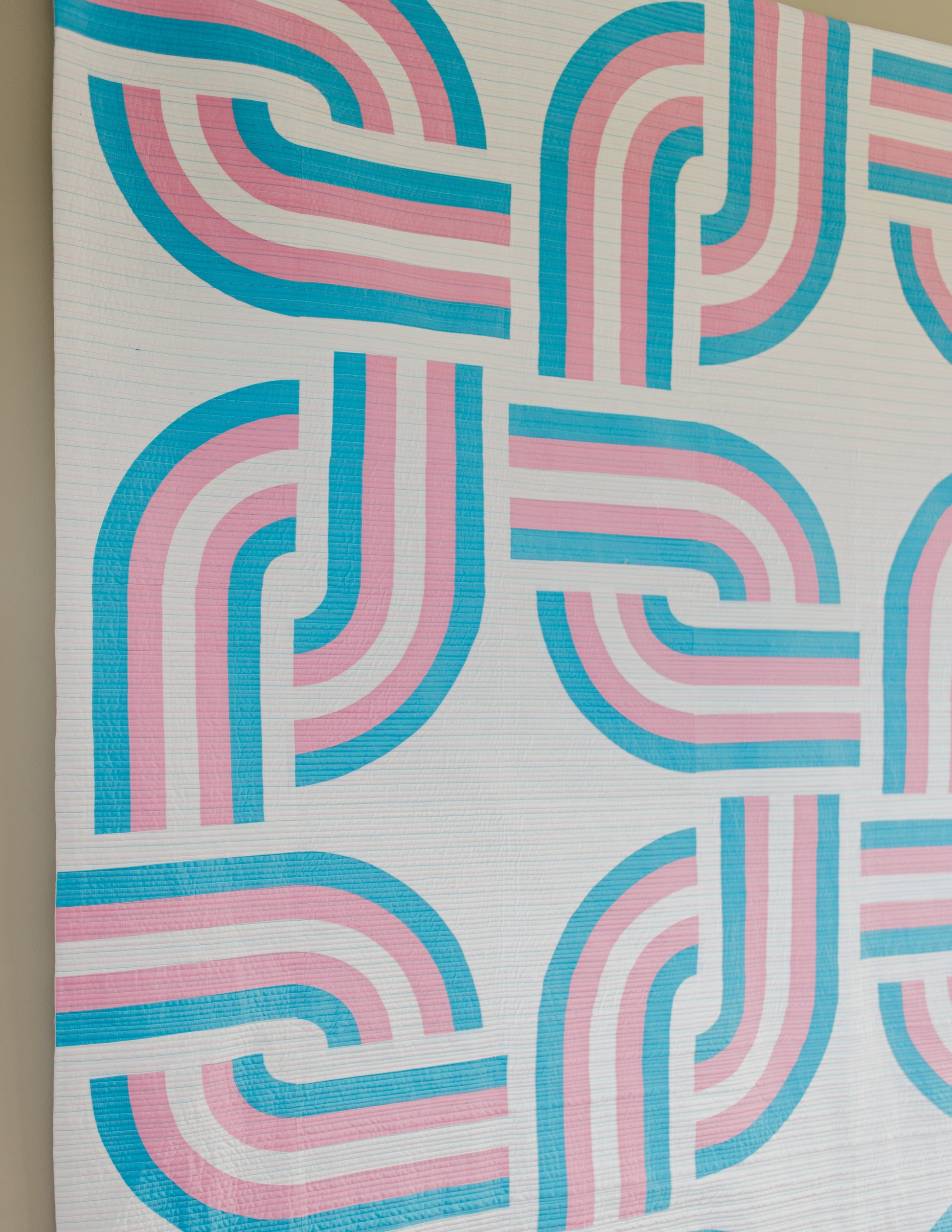 Close up view of quilt with pink and blue wavy pattern on a neutral background