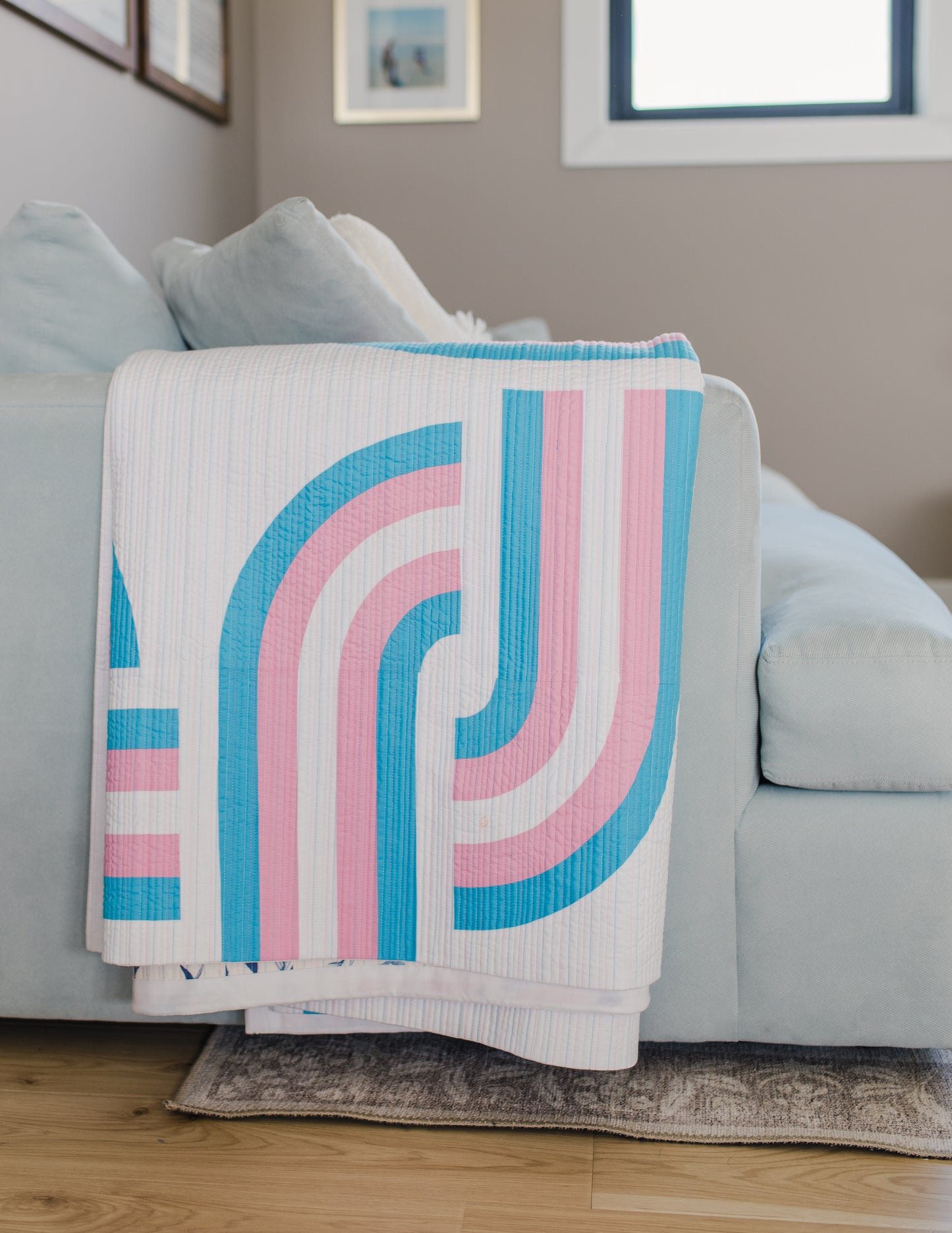 Decorative quilt with pink and blue stripes draped over a light gray sofa in a living room.