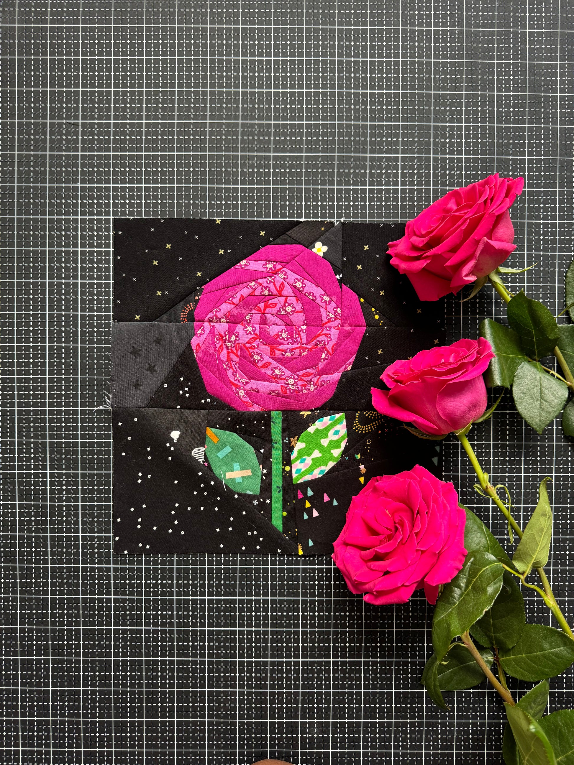 Artistic depiction of a pink rose with green leaves on a black background, surrounded by real pink roses.